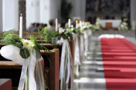 Blick auf eine festlich geschmückte Kirche mit Rosen und Kerzen entlang des Mittelgangs.