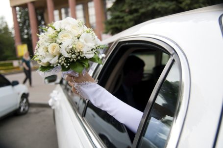 Eine Hand mit einem Hochzeitsstrauß hängt aus dem Fenster eines weißen Autos.