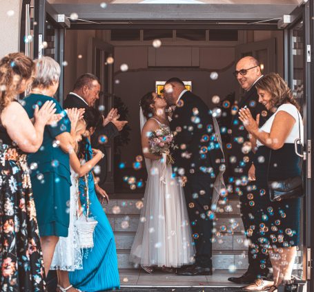 Brautpaar küsst sich bei der Hochzeit, umgeben von jubelnden Gästen und Konfetti.