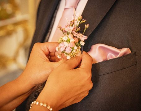 Eine Hand befestigt eine florale Ansteckblume an einem Anzug mit einer rosa Krawatte.