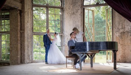 Hochzeitsfeier: Brautpaar steht in einem Raum, während ein Pianist spielt.