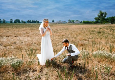 Braut und Bräutigam in einem trockenen Feld, umgeben von Gras und Blumen.