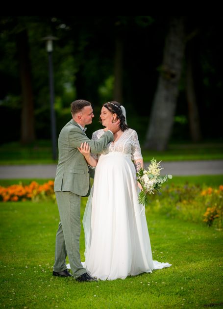 Braut und Bräutigam in eleganter Kleidung stehen in einem grünen Garten.